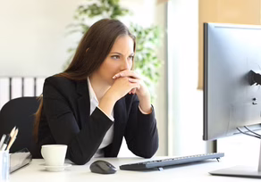 A woman in business attire thoughtfully working at her computer.