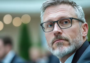 Thoughtful man with glasses looking away in a blurred outdoor setting.