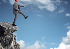 Man in a suit stepping off a cliff into the sky.