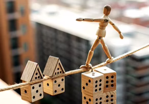 Wooden mannequin balancing on dice and houses.