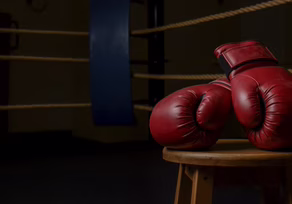 Red boxing gloves resting on a wooden stool in a dimly lit boxing ring.